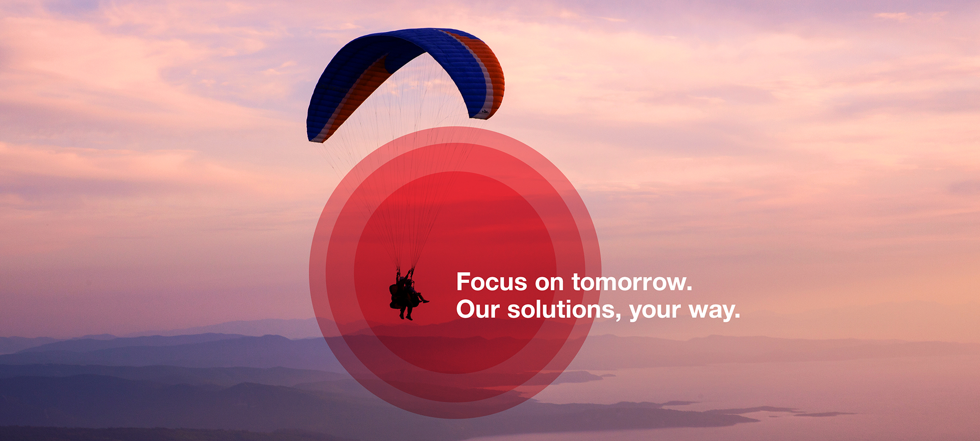 A soothing photograph of a paraglider flying in a beautiful landscape at sunset.